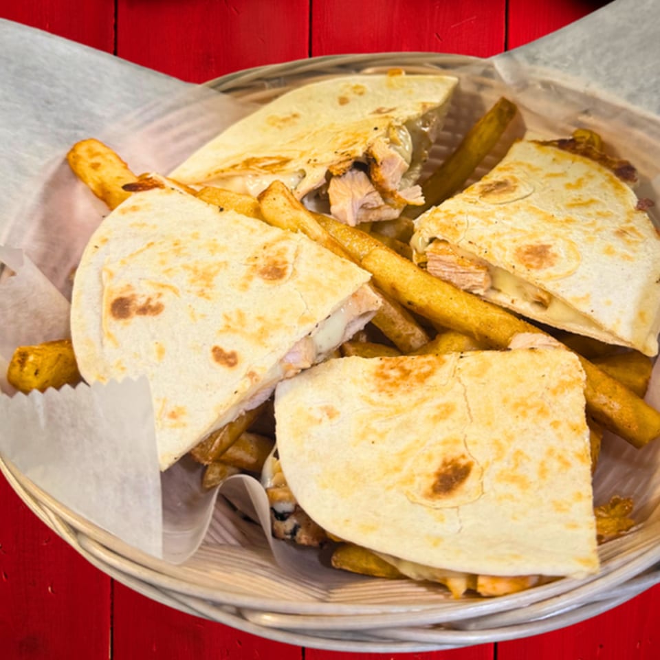 Chicken quesadilla wedges and french fries in a basket with white paper lining.