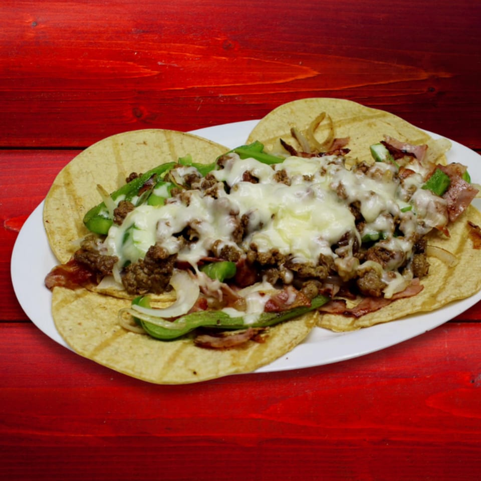 A plate of Gordito Tacos with melted cheese, ground meat, green peppers, and onions on a red wooden table.