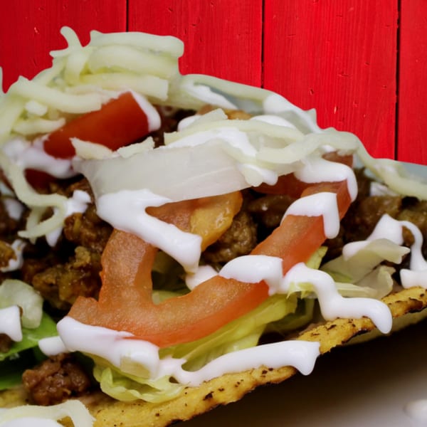 Close-up of a Gordito Tacos tostada with ground beef, lettuce, tomatoes, onions, cheese, and sour cream.