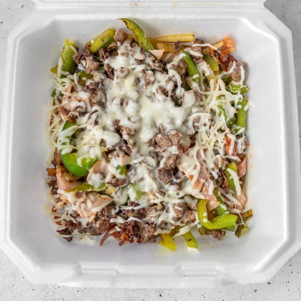 The Gordito Tacos' steak fajita fries, topped with melted cheese, green peppers, and onions in a white takeout container.