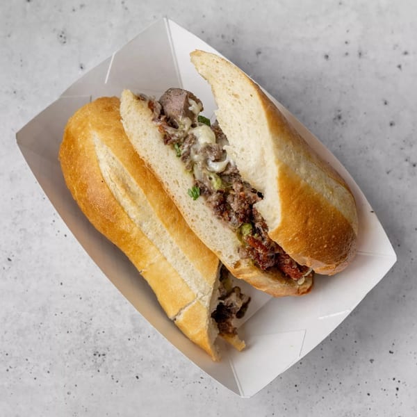 A Gordito Tacos Mexican sandwich, cut in half, filled with meat, cheese, and green herbs in a white paper tray.