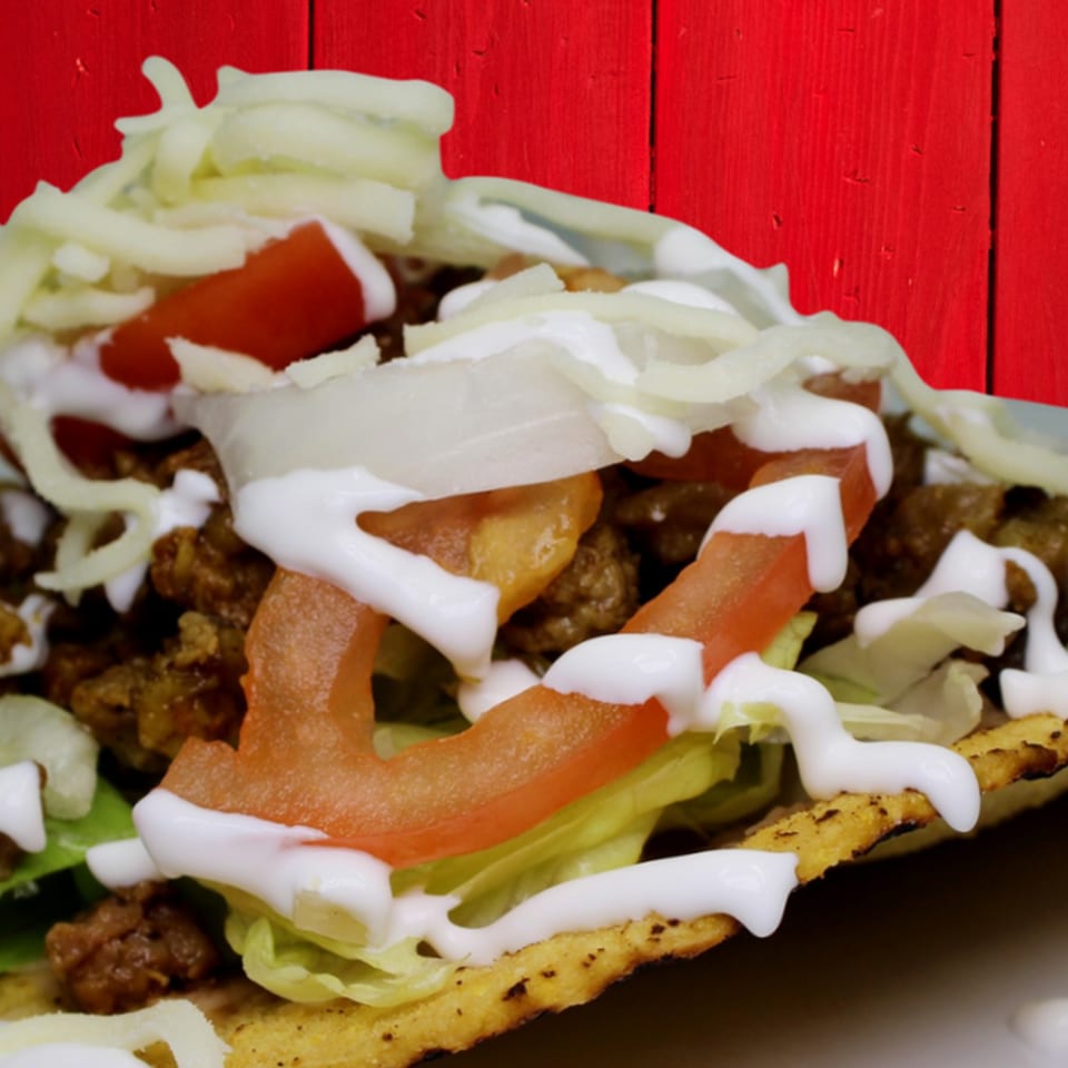 A Gordito Tacos taco filled with meat, lettuce, tomatoes, onions, cheese, and sour cream.