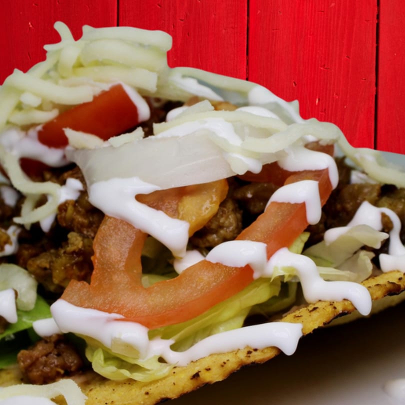 A Gordito Tacos taco filled with meat, lettuce, tomatoes, onions, cheese, and sour cream.