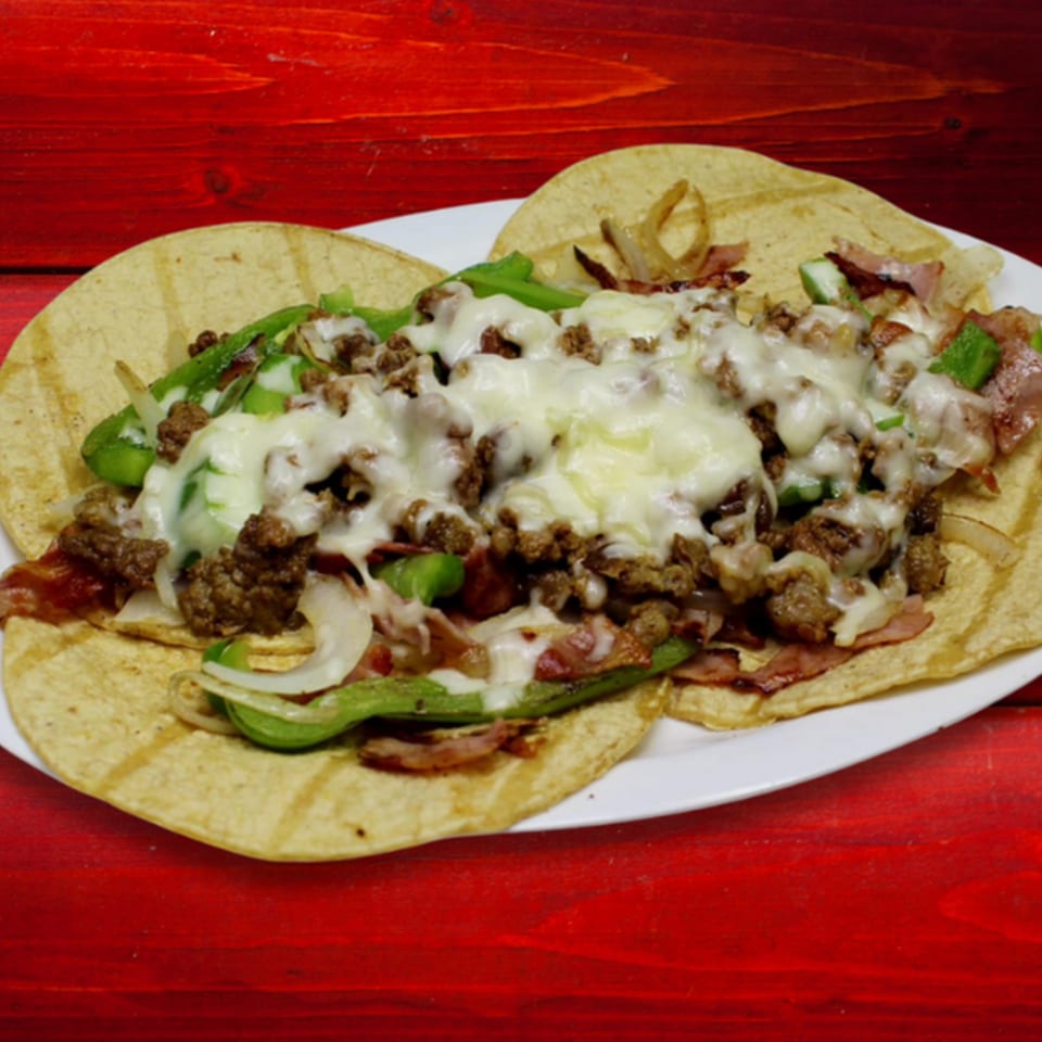 Two Gordito Tacos with melted cheese, ground meat, green peppers, and onions on a white plate.