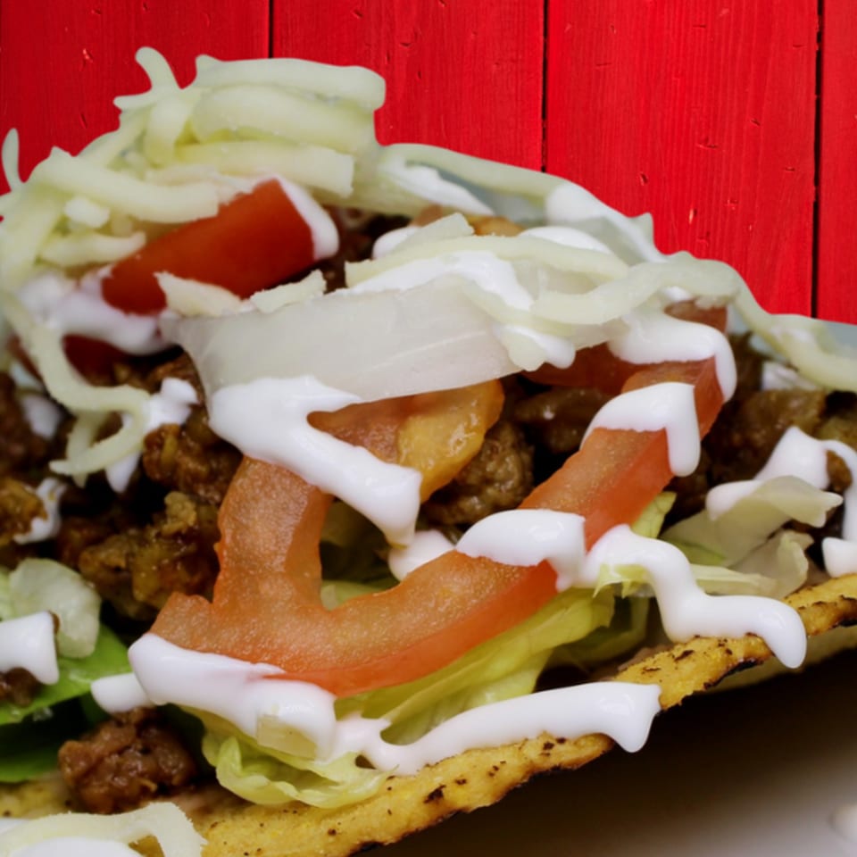 Close-up of a Gordito Tacos taco with ground beef, lettuce, tomatoes, cheese, and sour cream.