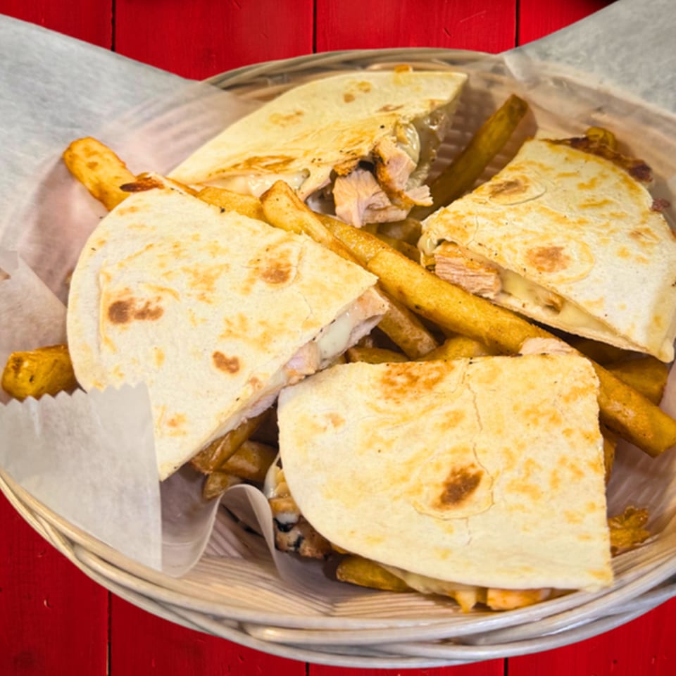 Chicken quesadillas and french fries in a basket with parchment paper on a red wooden table.